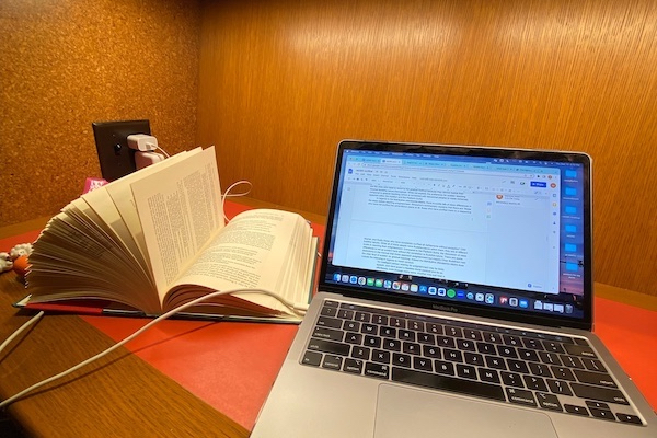 A desk with an open book and an Apple MacBook Pro displaying an opened Google document. 