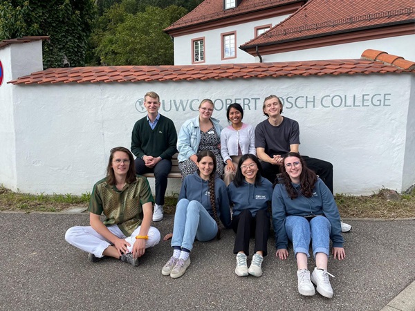 group of students pose seated in from of the white building with terracotta roof tiles